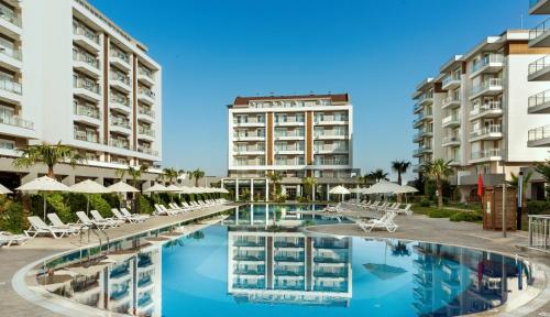 a pool with chairs and umbrellas in front of buildings at Greenwood Suites Resort in Lara