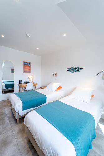 two beds in a white room with a desk at Hôtel La Chaumière-Les Pastourelles in Capbreton