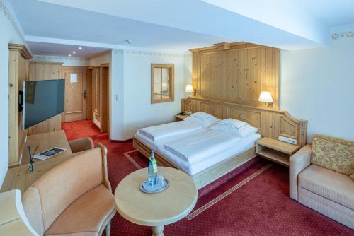 a bedroom with a bed and a couch and a tv at Natur & Alpinhotel Post in Vent