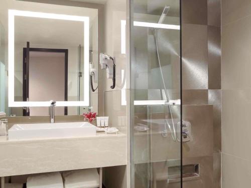 a bathroom with a sink and a mirror and a shower at Grand Mercure Medan Angkasa in Medan