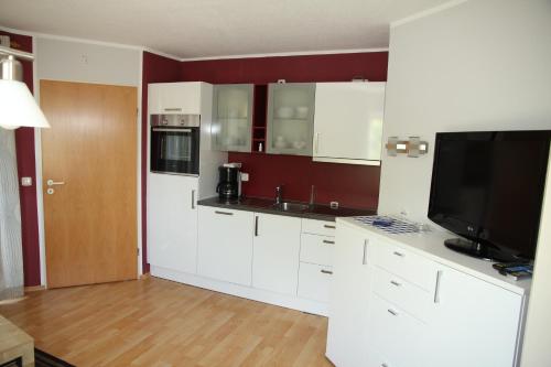 a kitchen with white cabinets and a flat screen tv at Ferienwohnung Gerda in Zandt