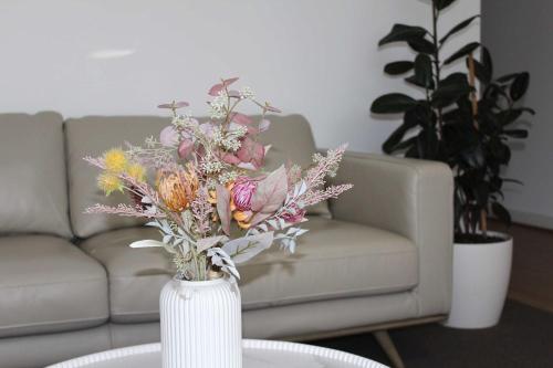 a vase filled with flowers on a table in front of a couch at Sunbury on the Park in Sunbury