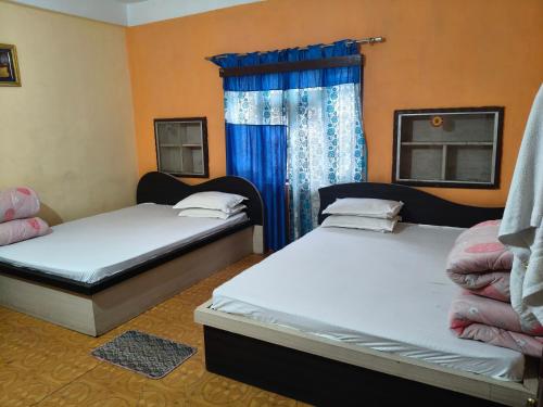 two beds in a room with blue curtains at Ilam Pahuna Ghar in Ilām