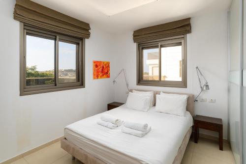a bedroom with a white bed and two windows at Mamad Comfort & Terrace In Ramat Aviv By Feelhome in Tel Aviv