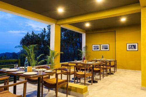a restaurant with tables and chairs and a large window at Rakkh Resort, a member of Radisson Individuals Retreats in Pālampur