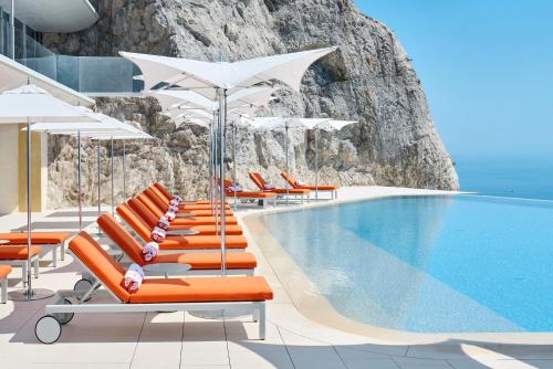 a swimming pool with orange lounge chairs and umbrellas at The Maybourne Riviera, Maybourne in Roquebrune-Cap-Martin