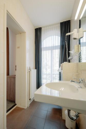 ein Badezimmer mit einem weißen Waschbecken und einem Fenster in der Unterkunft Parkhotel Lingen by Hackmann in Lingen