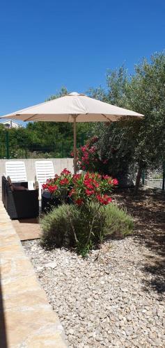 a patio with an umbrella and chairs and flowers at Marija Holiday Home in Sućuraj