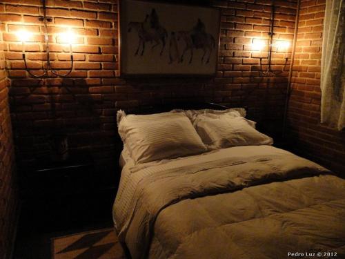 a bed with two lights on a brick wall at Pousada Romântica Serra da Mata in Penedo