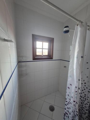 a white bathroom with a shower and a window at Morada Palmeira Real Peruibe - SP in Peruíbe