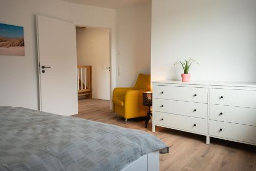 a bedroom with a white dresser and a yellow chair at Haus Wanger Meerblick in Wangerland