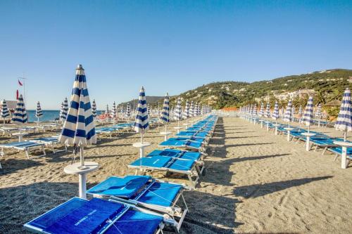 a row of blue chairs and umbrellas on a beach at Hotel Tirreno in Spotorno