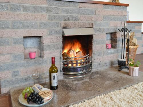 a brick fireplace with a plate of food and a bottle of wine at Beuchan Bungalow in Closeburn