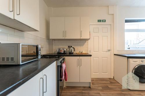 a kitchen with white cabinets and black counter tops at Holt House in Hindley