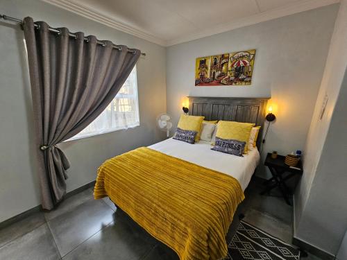 a bedroom with a bed with a yellow blanket and a window at PhysEQFiT Guesthouse in Centurion