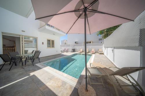 a house with a swimming pool and a pink umbrella at La Villa - Protaras in Paralimni