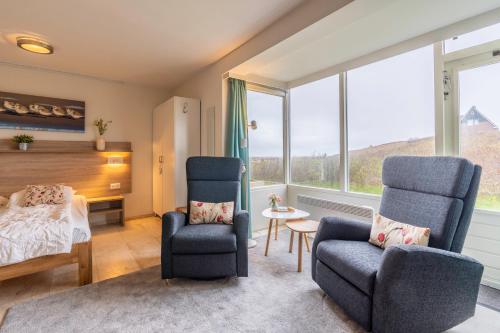 a bedroom with two chairs and a bed and windows at Appartementencomplex Juliana 68 in De Koog
