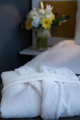 a white towel sitting on a bed with a vase of flowers at TAV Airport Hotel Izmir in Izmir