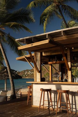 a bar on the beach with chairs and palm trees at Soho Beach House Canouan in Canouan