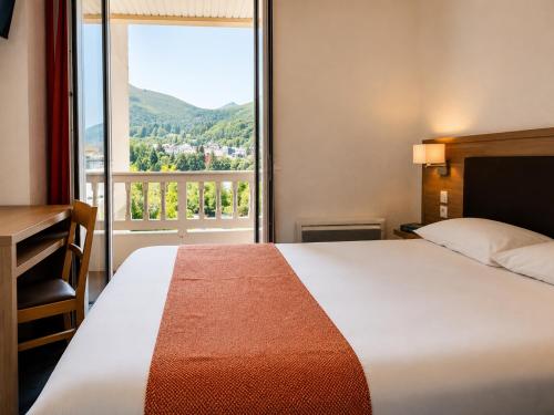 a hotel room with a bed and a large window at Hôtel Hélianthe in Lourdes