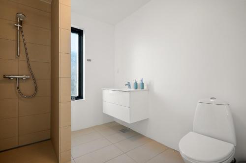 a white bathroom with a toilet and a shower at Sortehus - 100 steps from the finest beach in Vallebo