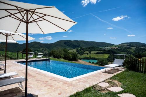a swimming pool with an umbrella and two chairs and a table at La Corte Sul Lago in Cingoli