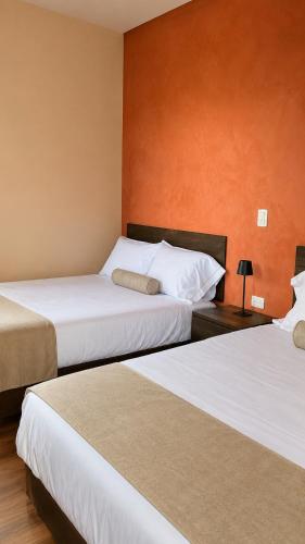 Zwei Betten in einem Hotelzimmer mit orangefarbenen Wänden in der Unterkunft Hotel Barrio Boutique in Monterrey
