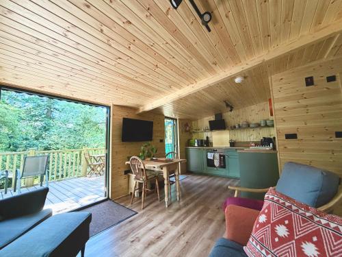 a living room with a wooden ceiling and a kitchen and a table at Lake District Woodland Cabin - Close to Ambleside & Langdale Valley in Ambleside