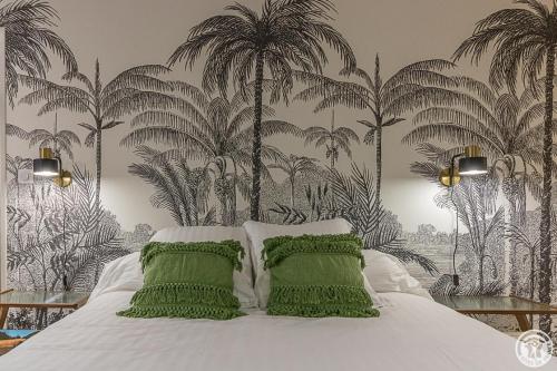 a bedroom with a bed with green pillows and palm trees at Le logis du lièvre in Lodes