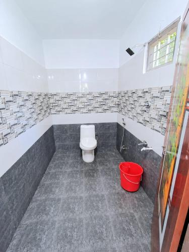 a bathroom with a toilet and a red bucket at munnar Green portico Cottages in Anachal