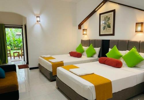 two beds in a room with green and orange pillows at Sunshine Resort Sigiriya in Sigiriya
