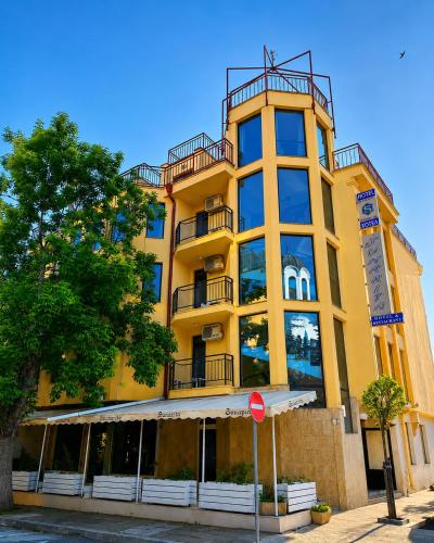 a tall yellow building with a tree in front of it at Хотел ЗОНАРИТА in Primorsko