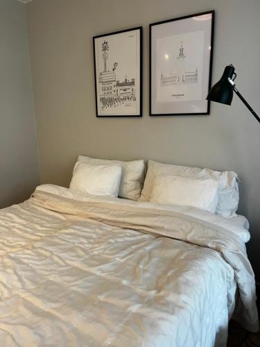 a bed with white sheets and two pictures on the wall at Perfect cosy living in Stockholm