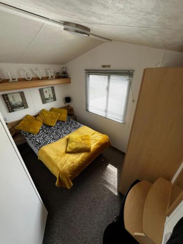 a bedroom with a bed with yellow sheets and a window at Izabela's Caravan - Caravan 261 in Saint Osyth