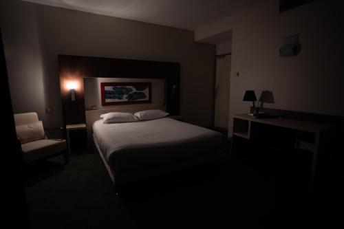 a bedroom with a bed and a chair in a dark room at Elema Hotels Beauvais ex Hostellerie Saint Vincent Beauvais Aeroport in Beauvais