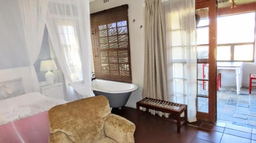 a bedroom with a tub and a bed and a chair at DeKotzenhof in Wakkerstroom