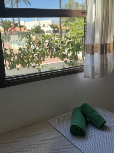 a green towel sitting on a bed next to a window at Los Porches K28 in Playa del Ingles