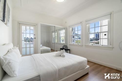a white bedroom with a large bed and windows at KozyGuru | MacMahons Point | Harbour Hideaway in Sydney