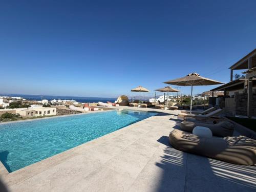 a swimming pool with chairs and umbrellas and the ocean at Ostria View Resort in Mikonos