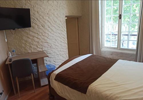 a bedroom with a bed and a desk and a television at Logis Hotel Restaurant La Chaumière in Tournon-sur-Rhône