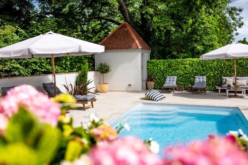 a swimming pool with two umbrellas and chairs and a patio at La Demeure du Bord'Ô in Lagruère