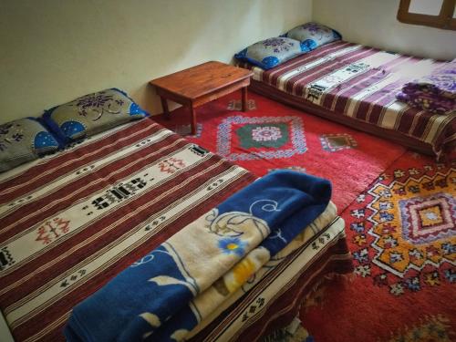 a room with two beds and a table and a tableasteryasteryasteryasteryastery at Gite Oussalem timichi in Timichchi