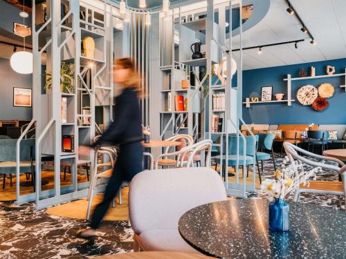 a woman walking past a table in a restaurant at Mercure Brest Centre Port in Brest