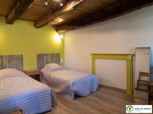 two beds in a room with yellow walls and wooden ceilings at Gîte Le Cayrou in Saint-Just-sur-Viaur