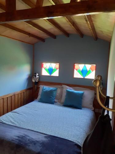 a bedroom with a bed with blue pillows and stained glass windows at The Cosy Nest Hut in Keddington