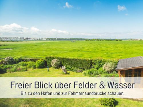 a large green field with a house in the foreground at Huus Binnensee OG2 - Dachwohnung mit Wasserblick - Lesesessel & WLAN - Für Paare - Ruhige Lage - Südstrand 5 Min mit Rad in Fehmarn