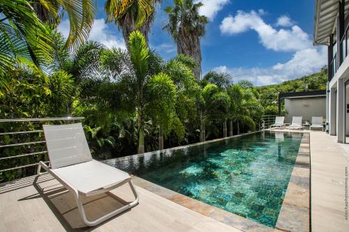 a swimming pool with a chair and palm trees at Karibu House in Les Trois-Îlets