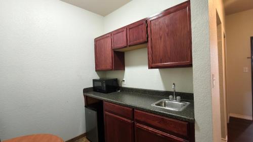 a small kitchen with wooden cabinets and a sink at Studio 7 By Capital O Killeen I-14 in Harker Heights