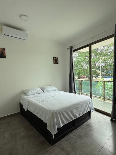 a white bedroom with a bed and a large window at Hotel Kleos in Cárdenas