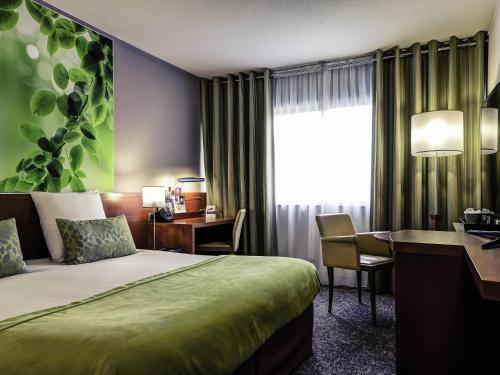 a hotel room with a bed and a desk and a window at Mercure Lyon Charbonnières in Charbonnières-les-Bains